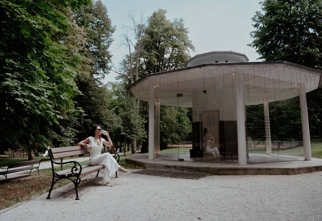 Paviljon pitnika termalne vode v Zdraviliškem parku z gostjo na klopi.